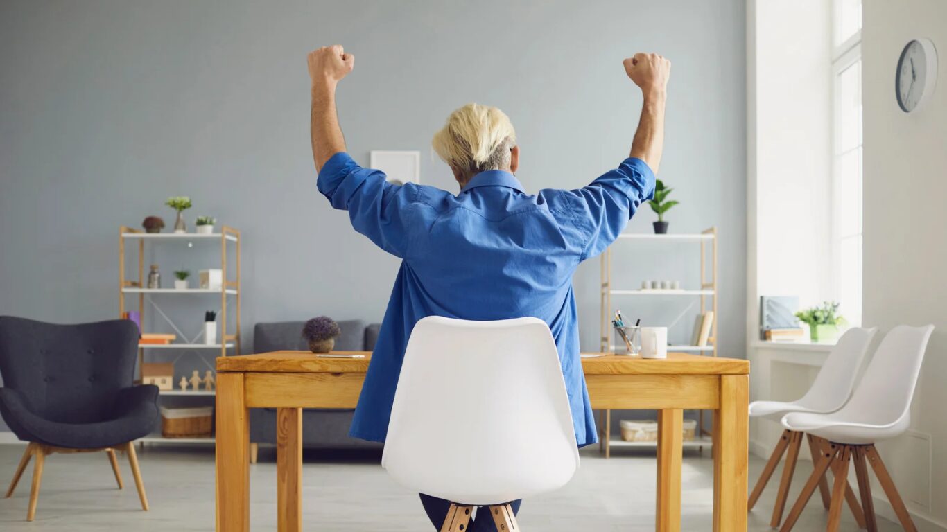 Frau sitzt am Schreibtisch und freut sich weil sie keine Schmerzen hat